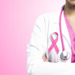 zdjęcie fragmentu tułowia kobiety w białym fartuchu z różową wstążką i stetoskopem na różowym tle