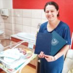 mama w oddziale z noworodkiem z tyłu w łóżeczkuz listem gratulacyjnym od Starosty Powiatu i ze szpitala w granatowych teczkach