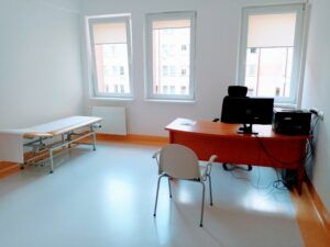 wnętrze jednego z gabinetów lekarskich w POZ z widokiem na biurko i kozetkę dla pacjenta